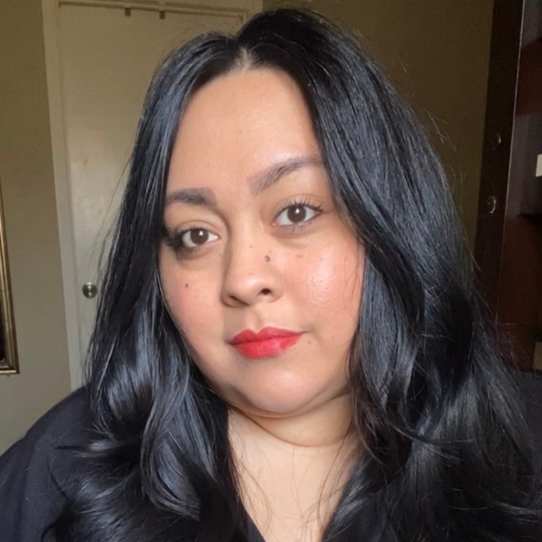 Woman with dark skin applying Reillie Beauty Organic Lipstick in Daylily, vibrant red shade with nourishing botanicals