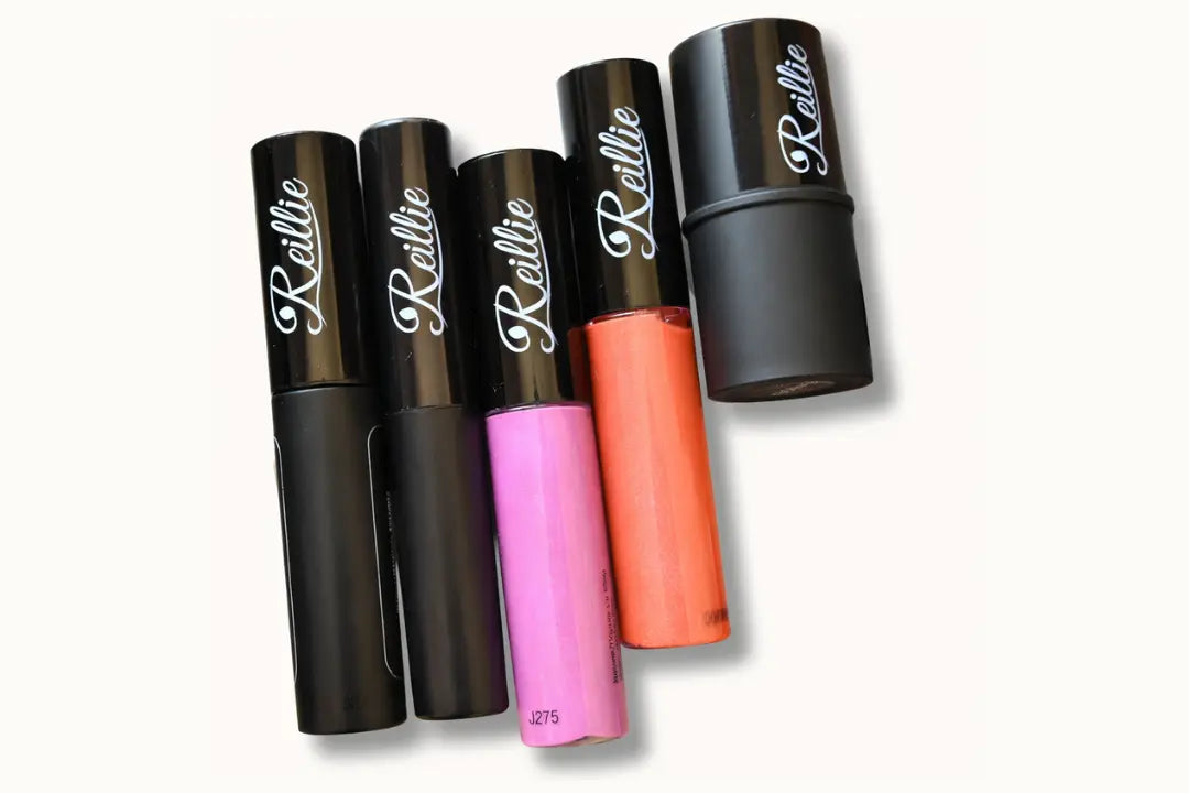 Makeup products including mascara, lip glosses in various shades, and a cheek tint arranged on a light background.