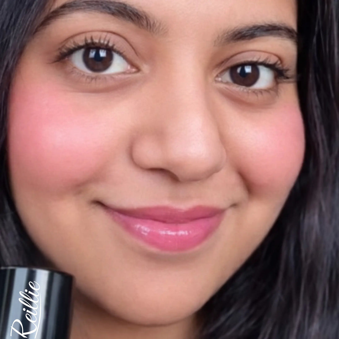 Woman applying Reillie Beauty Organic  tint in dahlia on face, soft pink shade for medium dark skin tone
