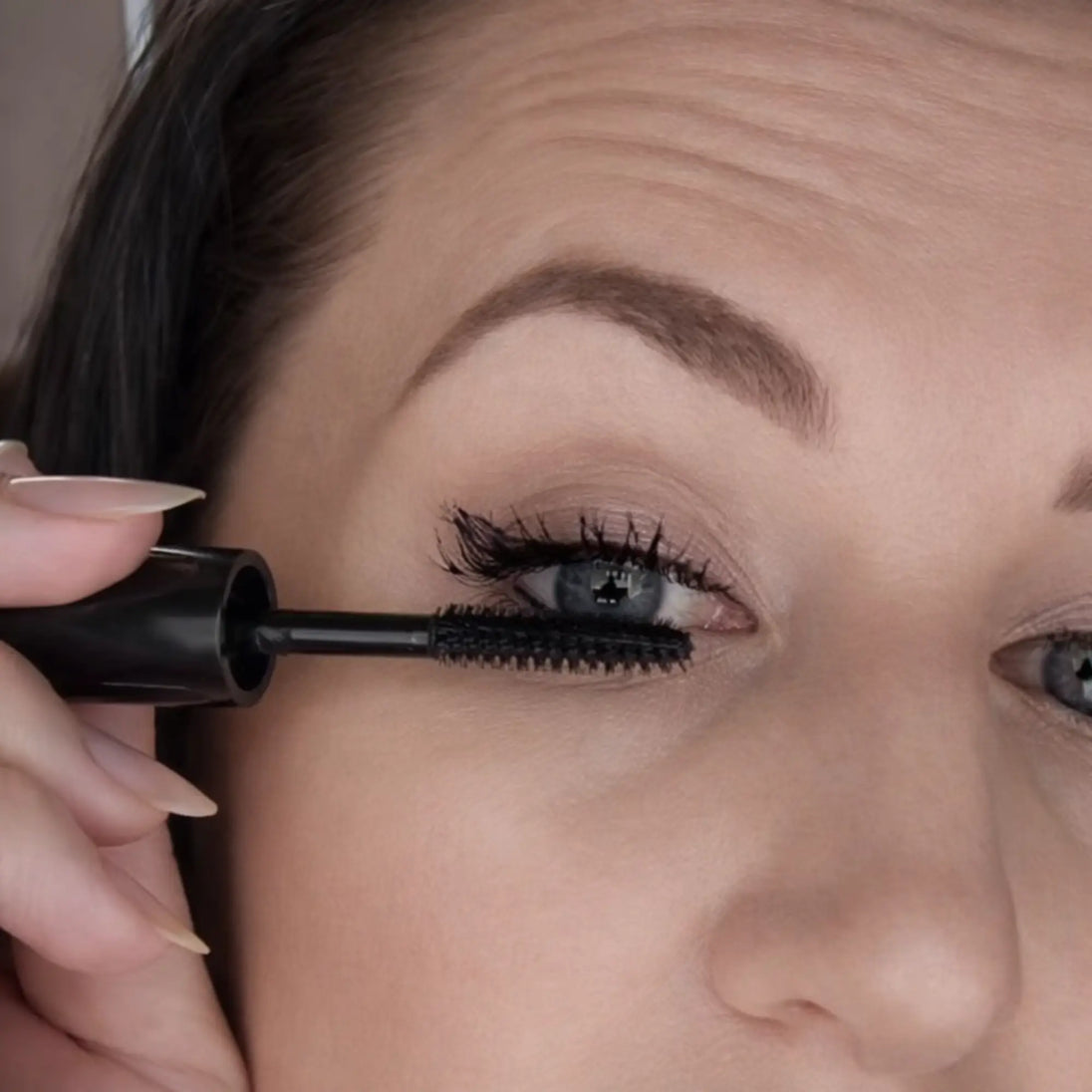 Close-up of a person applying mascara to their eyelashes.