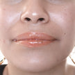 Woman with medium skin wearing caramel Lip Gloss, clear shimmering shade with nourishing botanicals