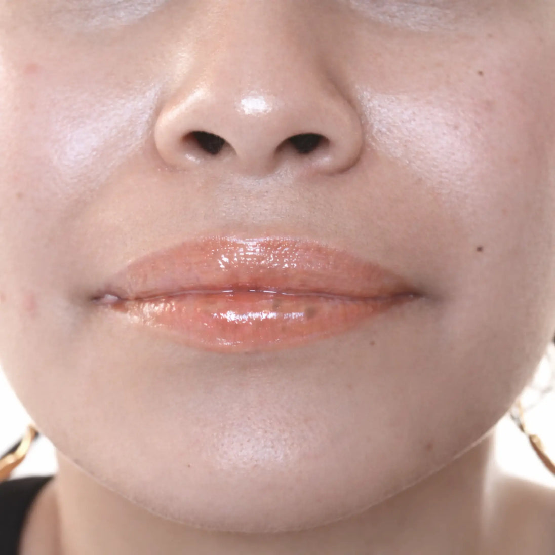 Woman with medium skin wearing caramel Lip Gloss, clear shimmering shade with nourishing botanicals