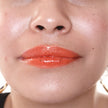 Woman with medium skin wearing cinnamon Lip Gloss, clear shimmering shade with nourishing botanicals