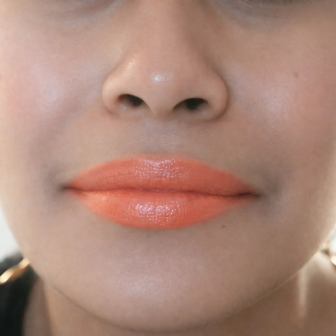 Woman with medium skin tone wearing Hyacinth Lipstick, orange shade with nourishing botanicals